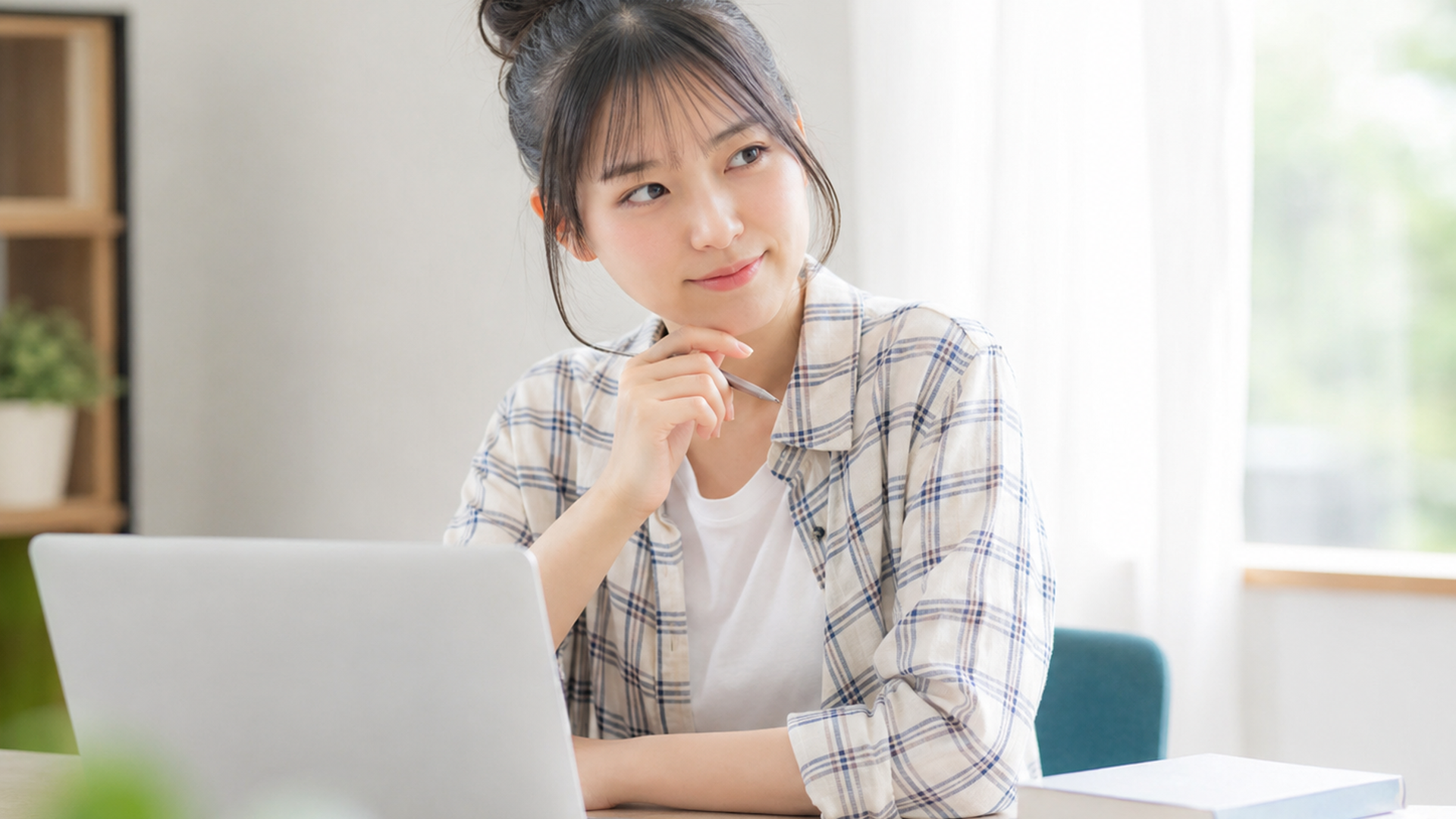 ノートPCとスマホを机に置き、参考書の横で副業について考える大学生